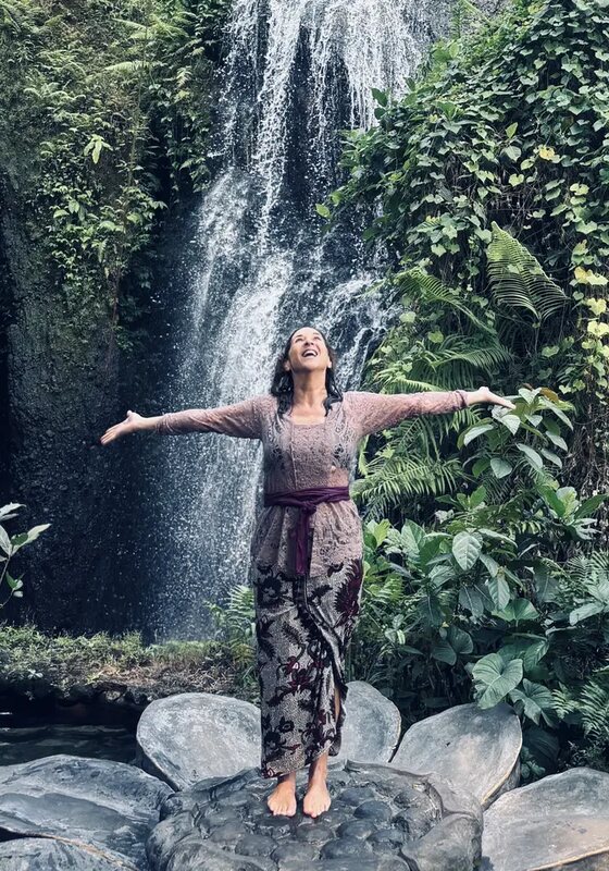 Julie Wright Halbert standing with her arms wide and her head back, a waterfall behind her